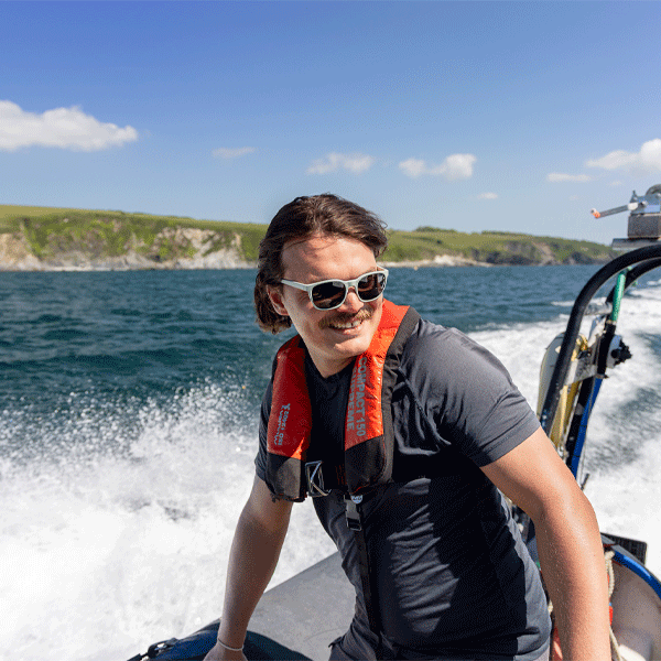 Man wearing sunglasses on a speedboat with rocky cliffs in background