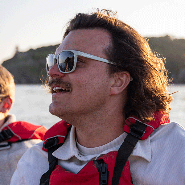 Man wearing pastel green sunglasses against an ocean background