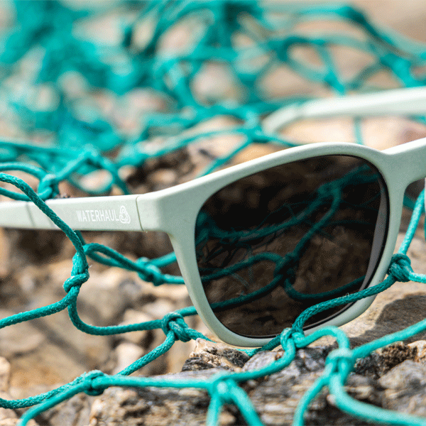 Close up of sunglasses with pale green frames and grey lenses with green fishing net in background