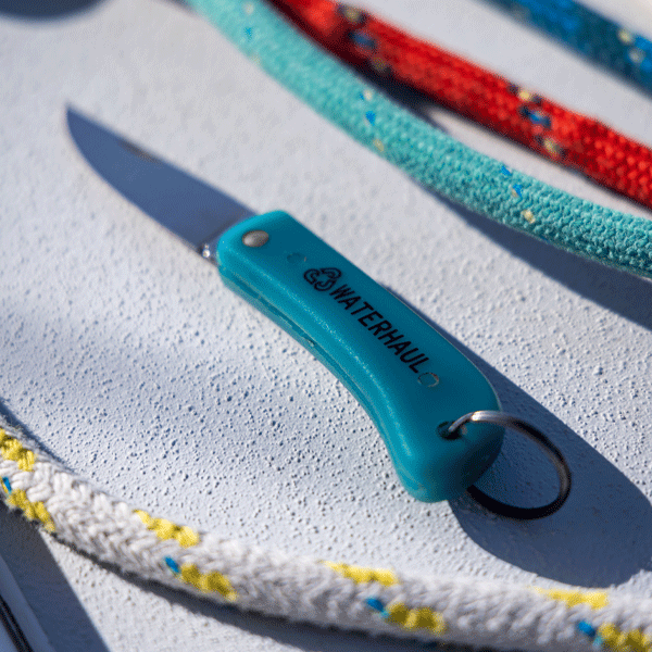 Pocket knife on white surface with coloured ropes in background