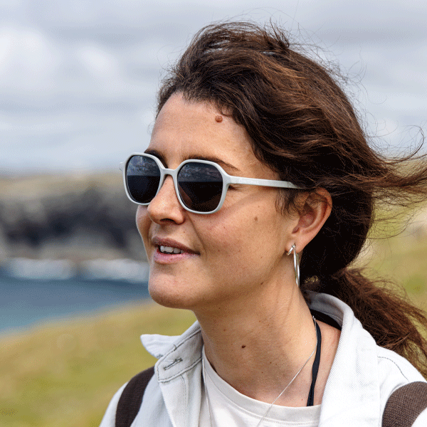 Woman wearing sunglasses with a scenic background of water and sky.