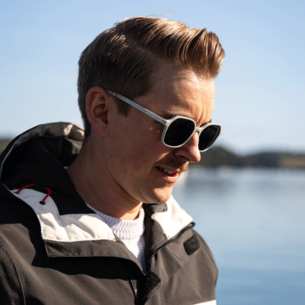 Man wearing sunglasses and a jacket by a body of water