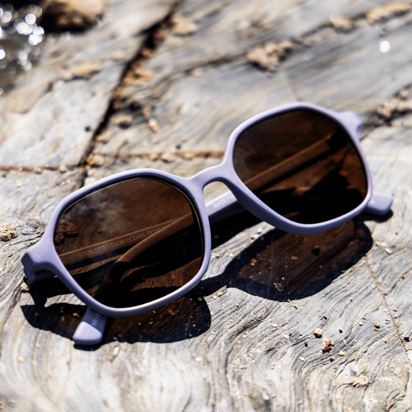 Pastel purple sunglasses with amber lenses on a rocky background