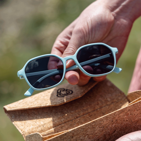 Hands removing light blue sunglasses for cork glasses case