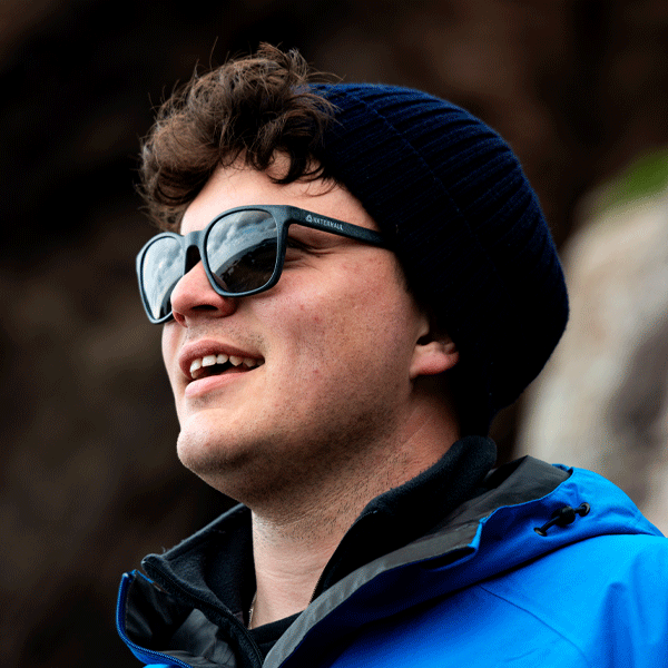 Man wearing sunglasses and a blue jacket with a blurred natural background