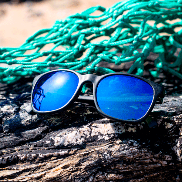 Blue sunglasses with reflective lenses on a rocky surface with green fishing net in the background