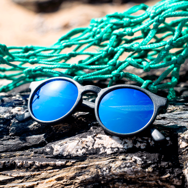 Round sunglasses with blue mirrored lenses on a rocky background with green fishing nets