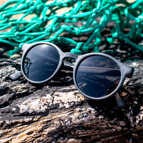 Round sunglasses with grey lenses on a rocky background with green fishing nets