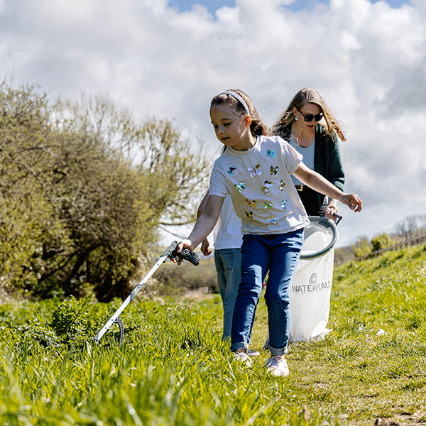 Two people walking through a grassy field using litter pickers to collect rubbish.