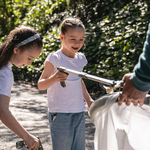 Two young girls using litter pickers outdoors, surrounded by greenery.