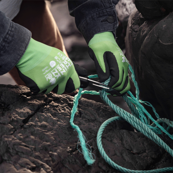 Person wearing green gardening gloves cutting green rope on a rocky surface