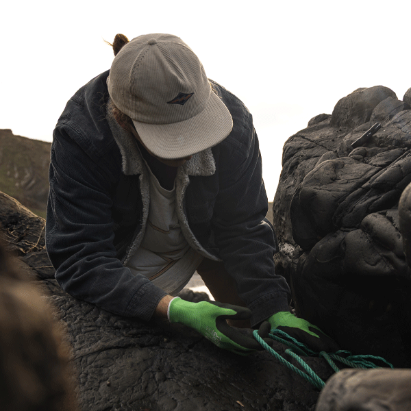 Person wearing a cap and gloves pulling ropes free from rocks