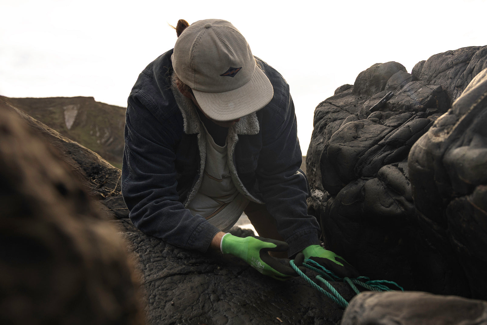 Person wearing a cap and gloves pulling blue rope from rocky crevice
