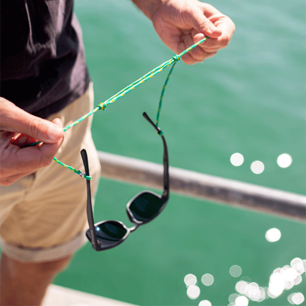 Person holding a sunglasses strap with sunglasses on a boat against a green water background