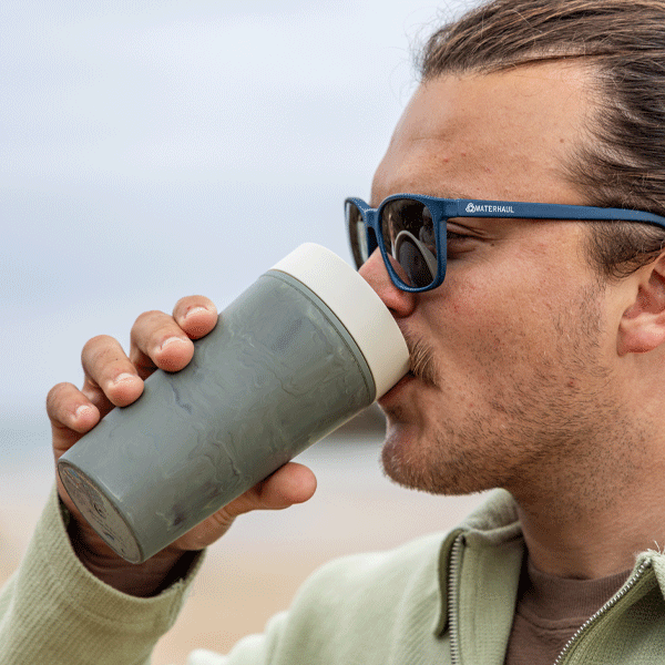 Man drinking from a green insulated mug outdoors
