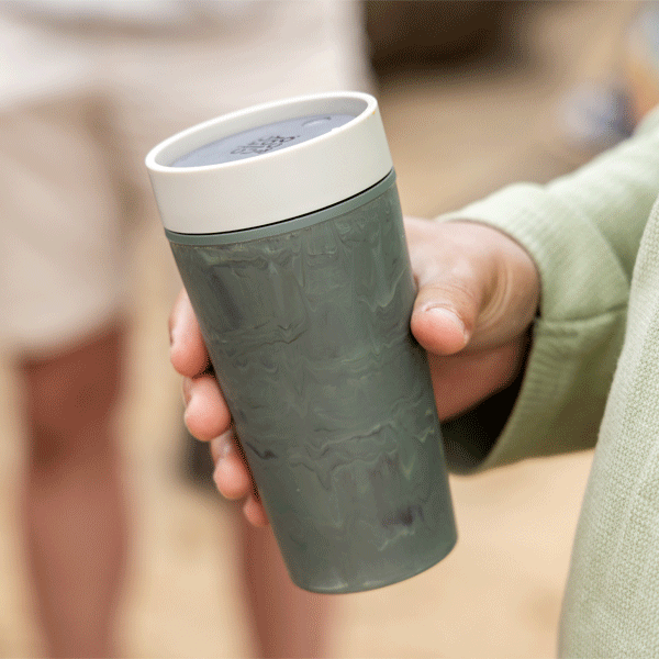 Person holding a textured grey coffee cup with a blurred background