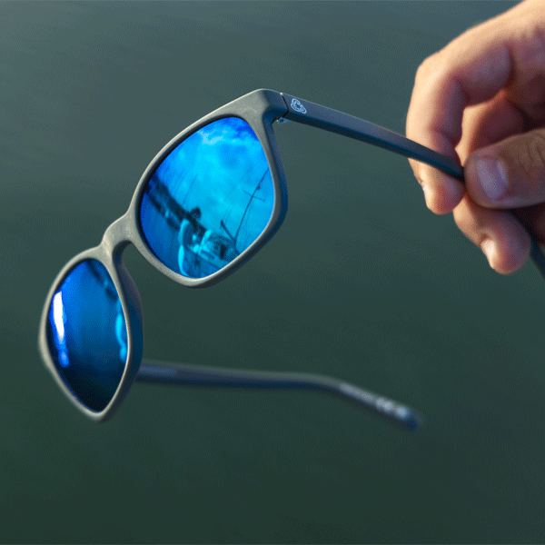 Blue reflective sunglasses held by a hand against a dark background